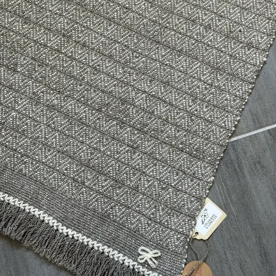 Tapis en pure laine naturelle Apportez une touche d'authenticité et de chaleur à votre intérieur avec ce tapis unique, entièrement tissé à la main sur métier à bras traditionnel par l'artisane Line PARERA. Véritable hommage au savoir-faire artisanal et à la filière laine française, il arbore un élégant motif géométrique né de la rencontre de deux laines aux nuances brutes et non teintes : la blancheur douce de la laine Hampshire et le caractère authentique de la laine Tarasconnaise grise. Ses finitions soignées, soulignées par de délicates franges et une bordure tressée, en font une pièce de caractère, durable et écoresponsable.