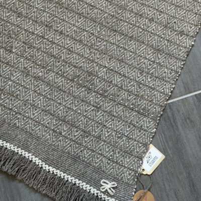 Apportez une touche d'authenticité et de chaleur à votre intérieur avec ce tapis unique, entièrement tissé à la main sur un métier à bras traditionnel par l'artisane Line PARERA. Confectionné à partir de laines locales non teintes, il associe la douceur de la laine cardée mérinos d'Arles (blanc naturel) à la texture authentique de la laine cardée tarasconnaise (grise). Son tissage minutieux révèle un subtil motif géométrique en losanges, sublimé par de généreuses franges torsadées. Caractéristiques : Dimensions : 140 cm × 68 cm (hors franges) Finitions : Franges torsadées de 20 cm Composition : 100% laine cardée locale (Mérinos d'Arles et Tarasconnaise) Fabrication : Artisanale française (8 heures de tissage)
