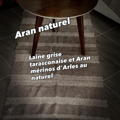 Apportez une touche d'authenticité et de chaleur à votre intérieur avec ce tapis unique, entièrement tissé à la main sur un métier à bras traditionnel par l'artisane Line PARERA. Confectionné à partir de laines locales non teintes, il associe la douceur de la laine cardée mérinos d'Arles (blanc naturel) à la texture authentique de la laine cardée tarasconnaise (grise). Son tissage minutieux révèle un subtil motif géométrique en losanges, sublimé par de généreuses franges torsadées. Caractéristiques : Dimensions : 140 cm × 68 cm (hors franges) Finitions : Franges torsadées de 20 cm Composition : 100% laine cardée locale (Mérinos d'Arles et Tarasconnaise) Fabrication : Artisanale française (8 heures de tissage)